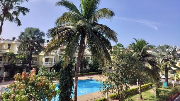 A pool surrounded by palm trees and a building with balconies. - Villa Neesham Grande (Benaulim)