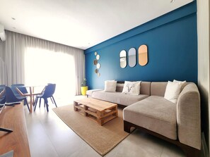Ein modernes Wohnzimmer mit blauer Akzentwand, einer Couch, einem Couchtisch und einem Essbereich mit Stühlen und Tisch.