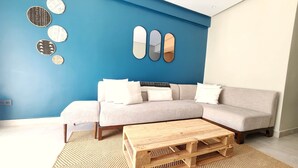Un salon moderne avec un mur d’accent bleu, un canapé d’angle gris, une table basse en bois et des miroirs décoratifs fixés au mur.