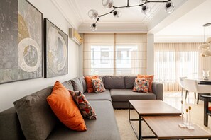 A modern living room with a grey sectional sofa, orange cushions, a wooden coffee table, and abstract wall art. - Number Six Triangle d'Or (Casablanca)