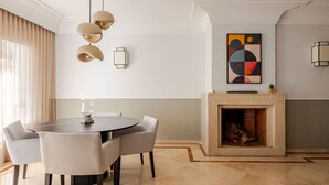Un espace repas moderne avec une table ronde, quatre chaises, des luminaires suspendus, une cheminée et un tableau abstrait accroché au mur.