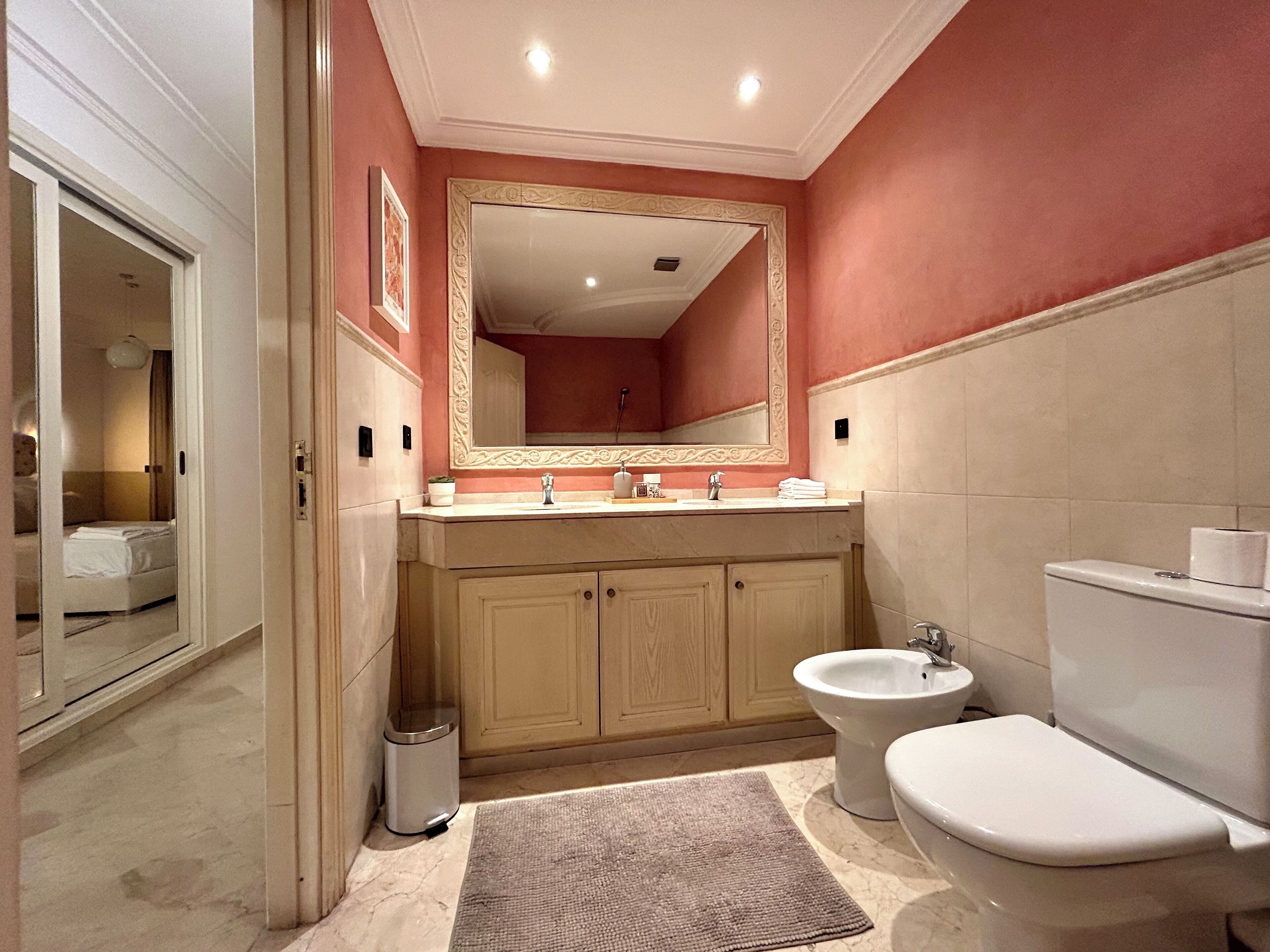 A modern bathroom with a beige vanity, a large mirror, a bidet, and a toilet.
