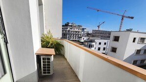 A balcony with a concrete floor, a small air conditioning unit, and a wooden ledge. In the background, there are buildings and construction cranes. - The 31 Grand Theatre by IB Signature - Spacious Art Deco 1 BR Apt. (Casablanca)