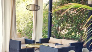 A covered outdoor seating area with wicker furniture, a round table, and a view of greenery. - Dar Bassidi by IB Signature - Luxury 5BR Villa -Heated Pool & Breakfast included (Marrakesh)
