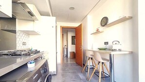 Une cuisine moderne équipée d’une cuisinière à gaz, d’appareils électroménagers en acier inoxydable et d’un coin repas avec une table et des chaises.