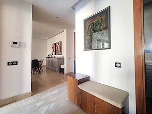 A modern interior with a wooden bench, a painting, and a kitchen area in the background. - C202 Alcazar - Modern 2BR flat by IB Signature (Casablanca)