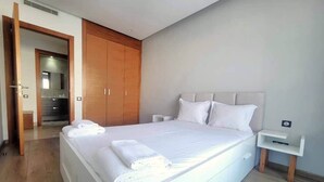 Une chambre moderne avec un grand lit, une armoire en bois et une petite table de chevet.