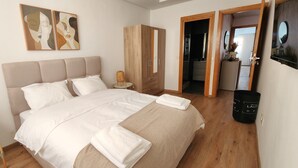 A bedroom with a large bed, a wardrobe, a small table with a basket, and a mirror on the wall. - Modern 2BR • 115m² • One-Five Racine by IB Signature (Casablanca)