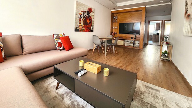 A modern living room with a sofa, coffee table, and a TV mounted on a wooden wall. - Modern 2BR • 115m² • One-Five Racine by IB Signature (Casablanca)