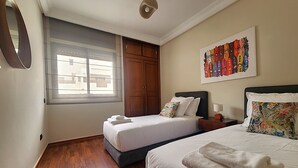 Ein Hotelzimmer mit zwei Betten, Holzboden, einem großen Fenster und einem farbenfrohen Kunstwerk an der Wand.