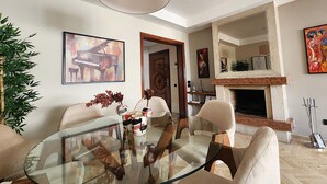 Ein modernes Wohnzimmer mit Glastisch, bequemen Sitzgelegenheiten, Kamin und Kunstwerken an den Wänden.