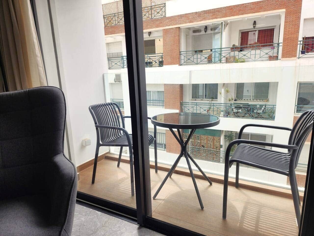 Een balkon met een ronde tafel en twee stoelen, met uitzicht op een gebouw met meerdere balkons.