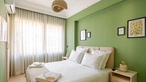 Ein ordentlich bezogenes Bett mit weißen Leinen, ein Nachttisch mit Lampe und ein gerahmtes Bild an der Wand.