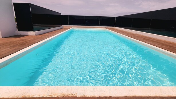 Ein rechteckiger Pool mit klarem, blauen Wasser, umgeben von Holzterrasse und weißer Umrandung.