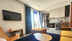 Ein modernes Wohnzimmer mit einer Couch, einem Hocker und einem an der Wand montierten Fernseher.