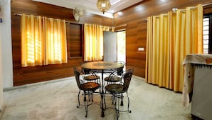 A dining area with a round table and four chairs, wooden panel walls, and yellow curtains. - Basil Inn near To Taj Mahal (Agra)