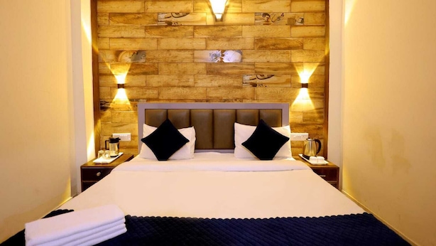 A hotel room with a wooden headboard, two bedside lamps, a bed with white linens, and a nightstand with a coffee pot. - Basil Inn near To Taj Mahal (Agra)