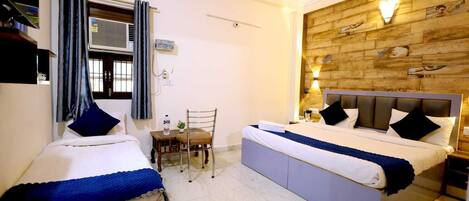 A hotel room with two beds, a small table with a chair, a window with curtains, and a wooden accent wall.