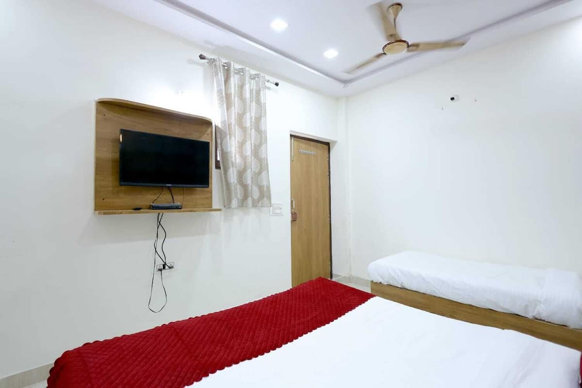 Un dormitorio con una cama, un televisor montado en la pared, un ventilador de techo y una puerta.