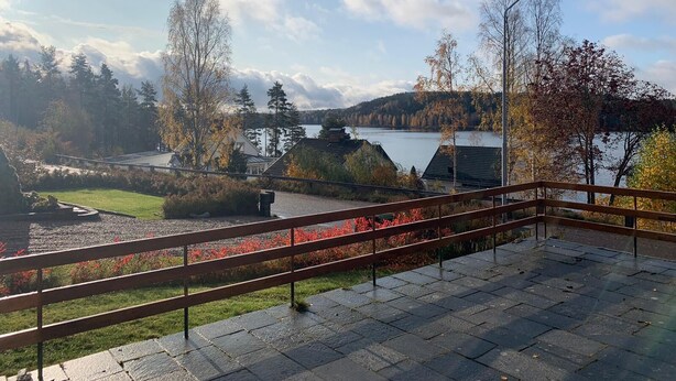 Vista desde un balcón sobre un lago, con baranda de madera y una zona pavimentada en primer plano.