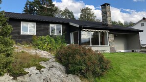 Una casa de dos pisos con chimenea de piedra, ventanas grandes y un porche de piedra.