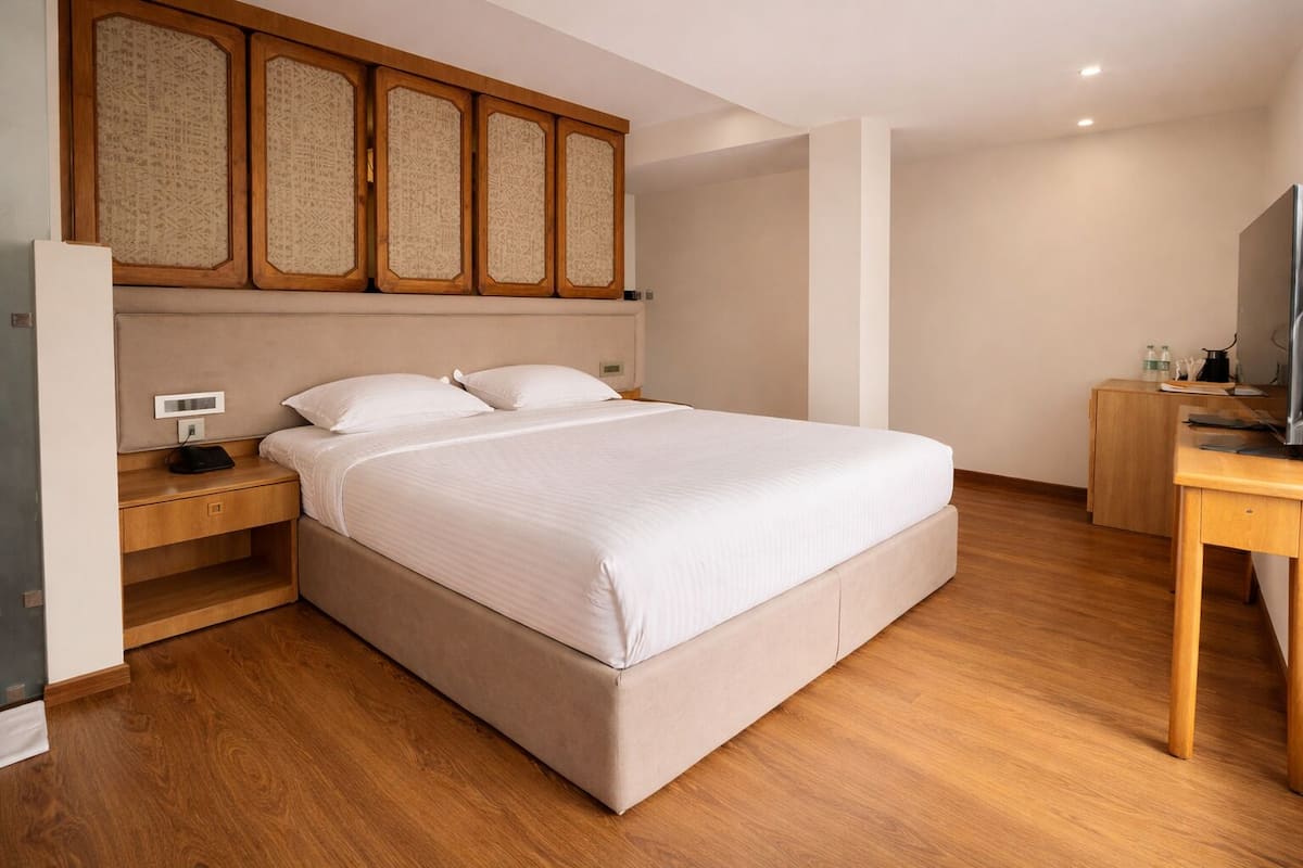 Ein Schlafzimmer mit einem Bett, Nachttischen aus Holz, einem Schreibtisch und einem Fernseher.
