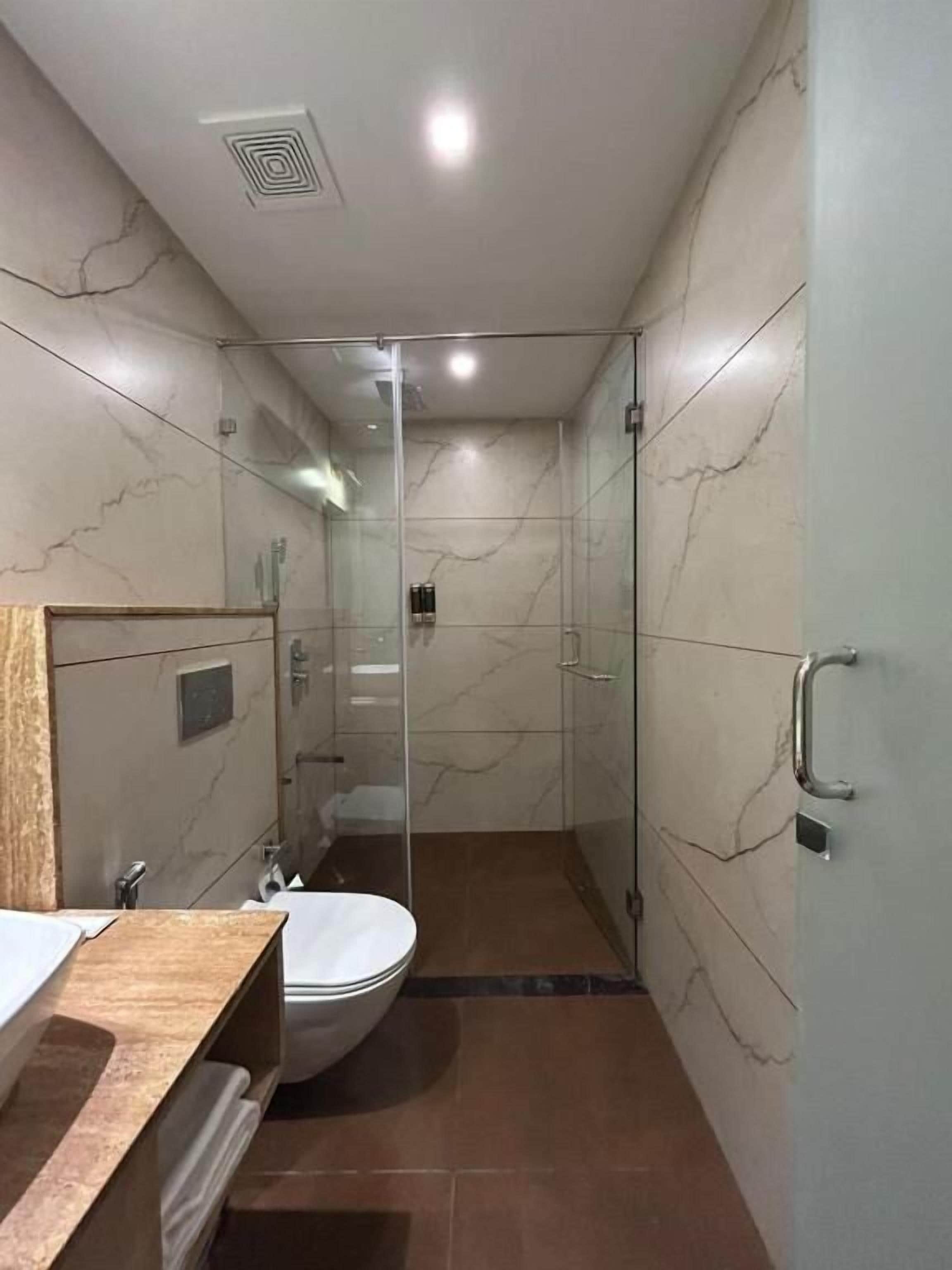 Un baño moderno con ducha de vidrio, pared de azulejos de mármol y tocador de madera.