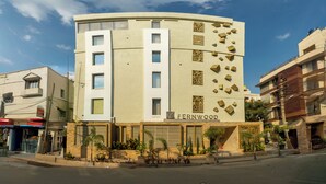 A multi-story building with a curved facade, a sign reading "FERNWOOD," and a small garden area with potted plants at the entrance. - FERNWOOD HOTELS AND RESORTS (Bengaluru)