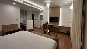 A modern hotel room with a large bed, a desk, a TV, and a bathroom with a mirror and sink. - FERNWOOD HOTELS AND RESORTS (Bengaluru)