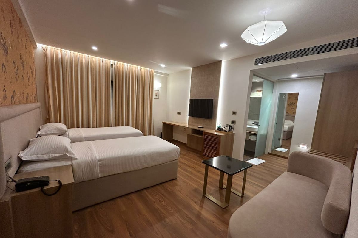 Ein modernes Hotelzimmer mit zwei Betten, einem Sofa, einem Schreibtisch und einem Fernseher.