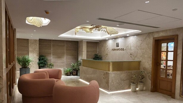 A modern reception area with a marble reception desk, two pink armchairs, and a ceiling sculpture. - FERNWOOD HOTELS AND RESORTS (Bengaluru)