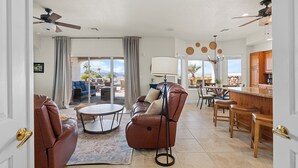 A spacious living room with a brown leather sofa, a round coffee table, and a dining area with wooden chairs and a bar. - The Sun Chaser, 4 bdr. Pool, Spa and Endless Views (Lake Havasu City)