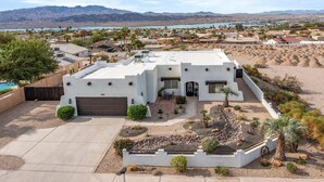 A modern house with a white exterior, a garage, and a landscaped front yard with palm trees and a small garden. - The Sun Chaser, 4 bdr. Pool, Spa and Endless Views (Lake Havasu City)