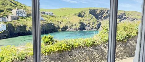 A coastal view with houses on a hillside, a rocky shoreline, and a clear sky.