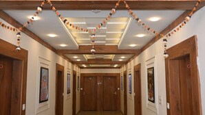 A hallway with wooden doors, framed artwork, and a ceiling with recessed lighting and decorative garlands. - Ramlala Hotel (Faizabad)