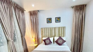 A bedroom with a bed, curtains, a headboard, and two framed pictures on the wall.