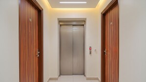 A hallway with wooden doors on either side, a central elevator, and a light strip above the elevator. - Hotel Church House - Rohini I Near Metro I Spacious Rooms I Friendly Staff I Most Preferred Hotel In Rohini (New Delhi)