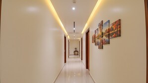 A long, well-lit hallway with a polished floor, wooden doors, and framed artwork on the walls. - Hotel Church House - Rohini I Near Metro I Spacious Rooms I Friendly Staff I Most Preferred Hotel In Rohini (New Delhi)