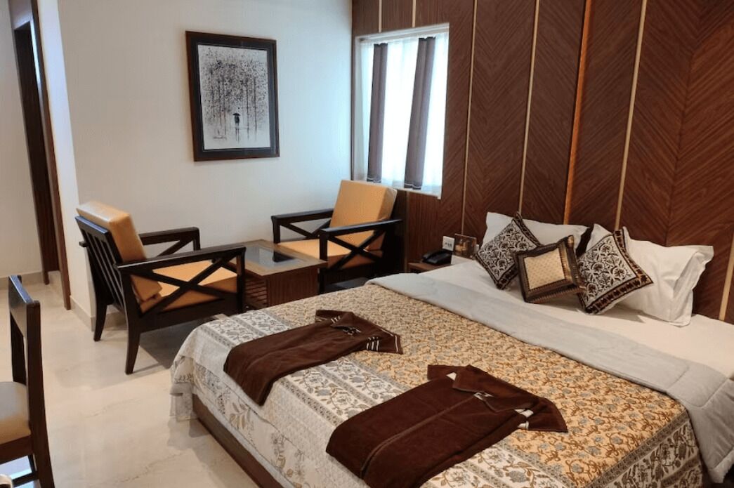 A bedroom with a large bed, two chairs, a nightstand, and a framed picture on the wall.