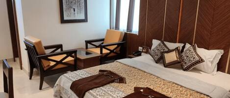 A bedroom with a large bed, two chairs, a nightstand, and a framed picture on the wall.