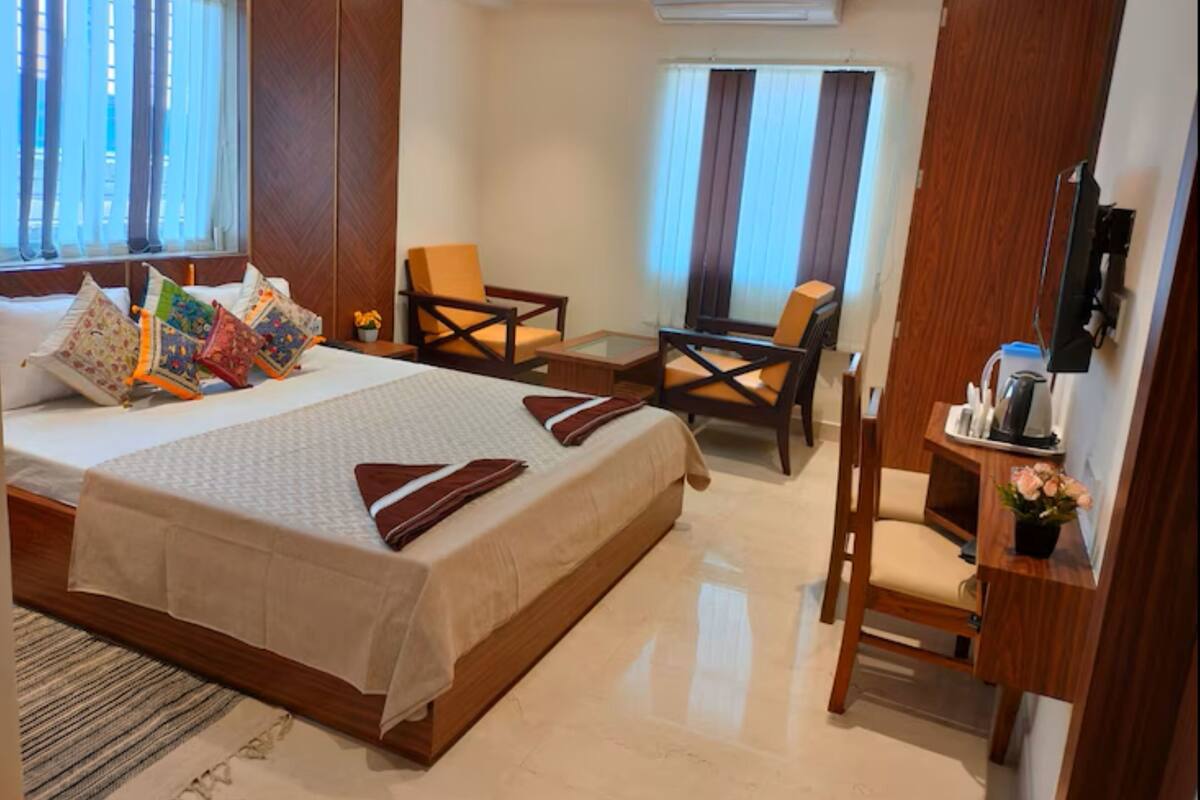 A hotel room with a large bed, two armchairs, a desk, and a TV.