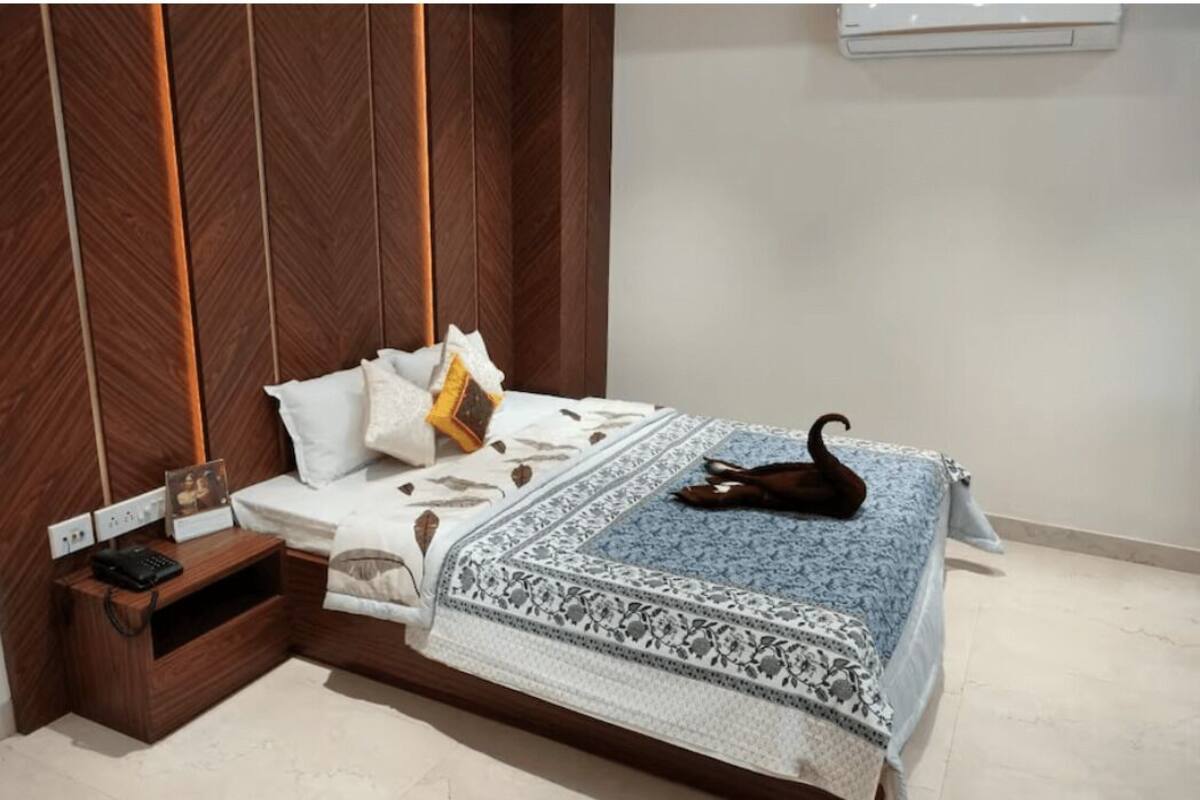A neatly made bed with a patterned bedspread, a bedside table with a lamp, and a wall-mounted air conditioner.