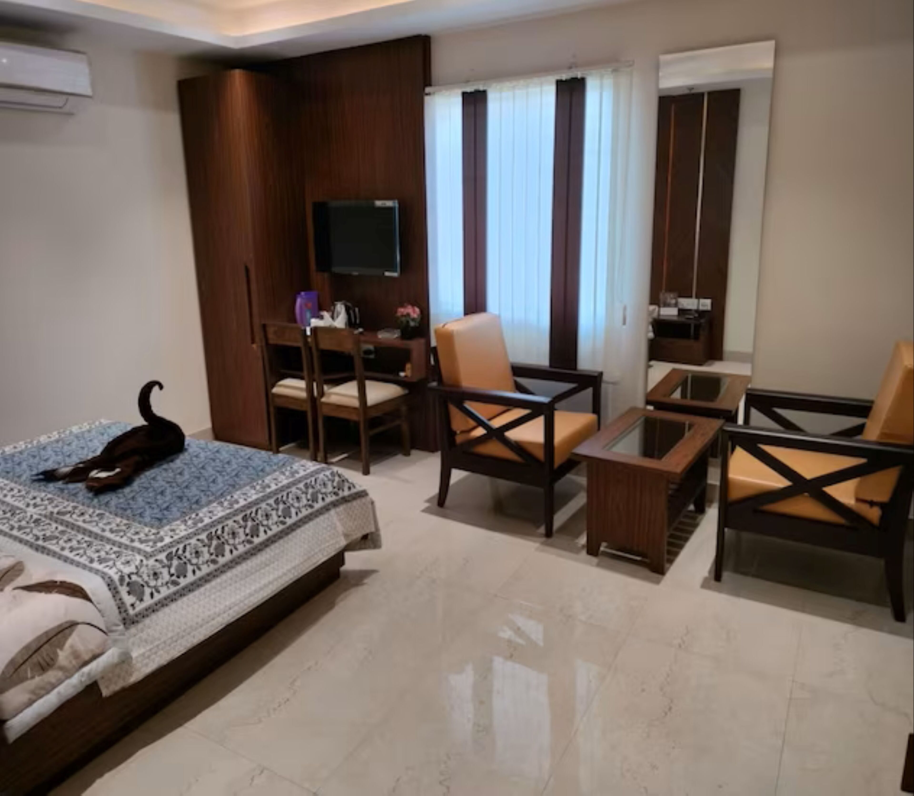 Une chambre d’hôtel comprenant un lit, deux fauteuils, un canapé, une télévision et une fenêtre avec des rideaux.