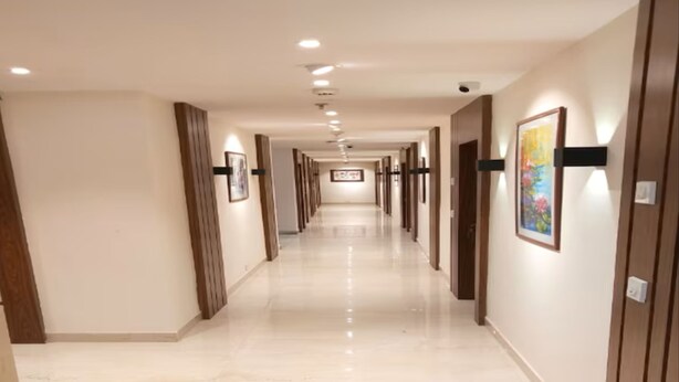 A hotel corridor with a polished floor, wooden paneling, and framed artwork on the walls. - Eennra Maanikko (Krishnanagar)
