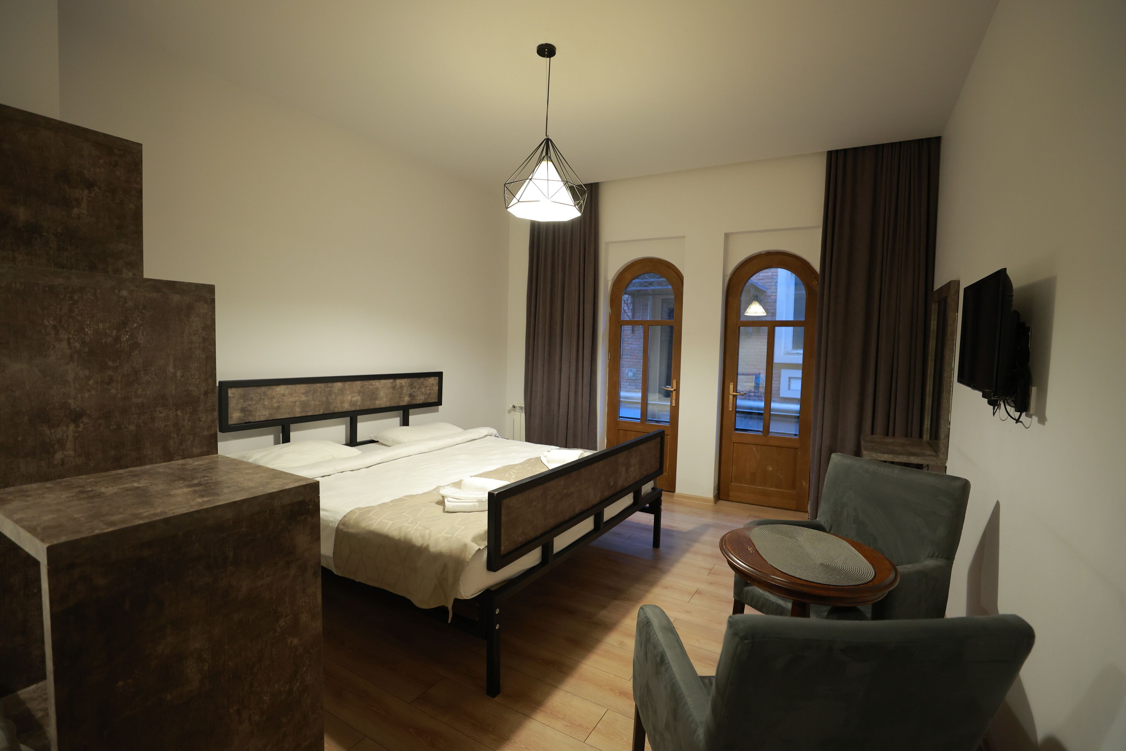 Un dormitorio con cama, una silla, un escritorio, un televisor y una ventana con cortinas.