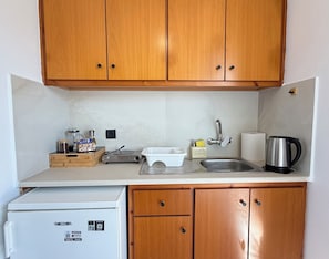 A compact kitchen with wooden cabinets, a stainless steel sink, a coffee maker, a kettle, and a small refrigerator. - Meltemi SeaView Suite (Kos)