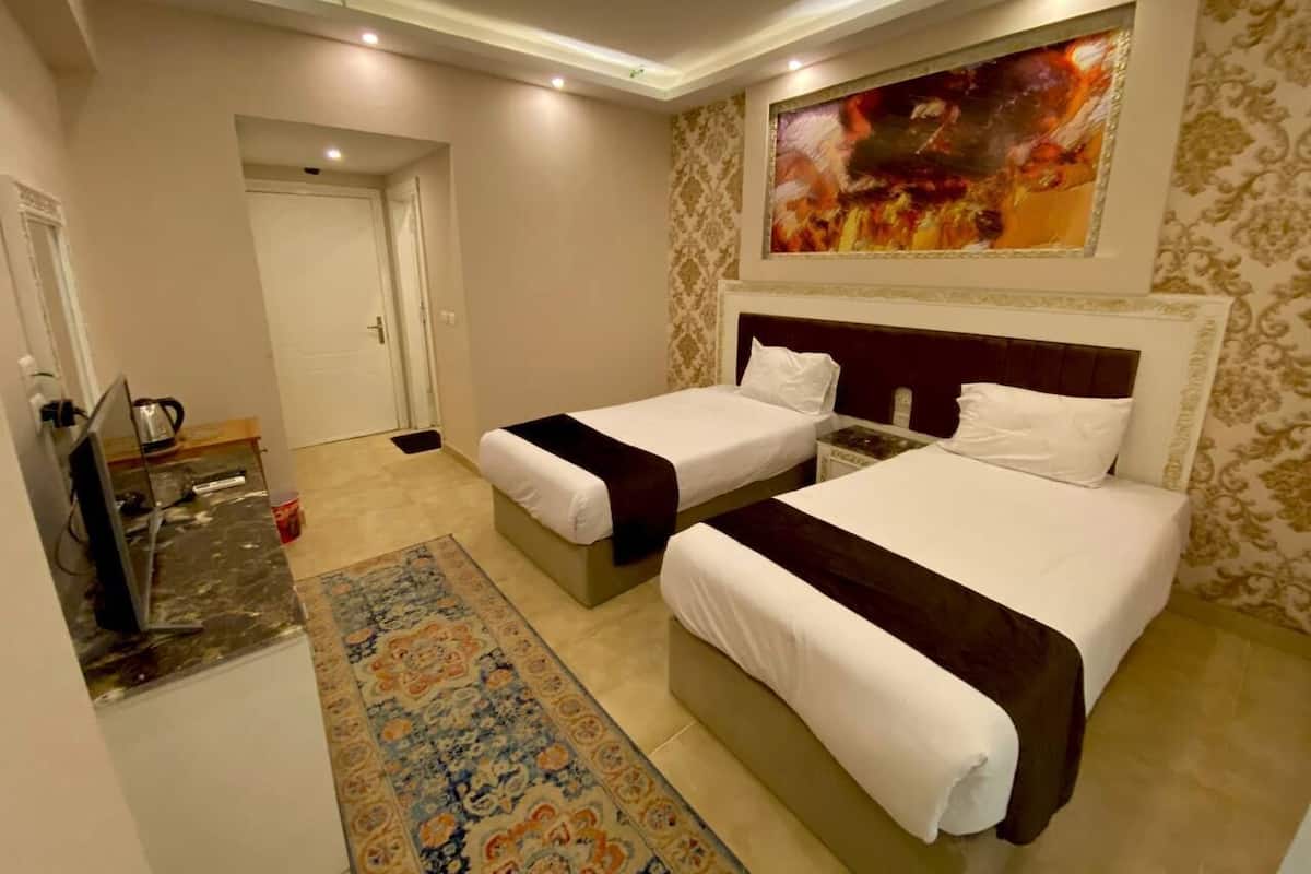 A hotel room with two beds, a TV, and a painting on the wall.