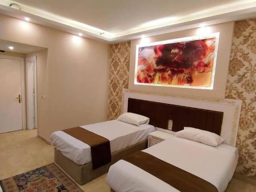 Habitación de hotel con dos camas, un cuadro abstracto grande sobre las camas y una alfombra estampada en el suelo.