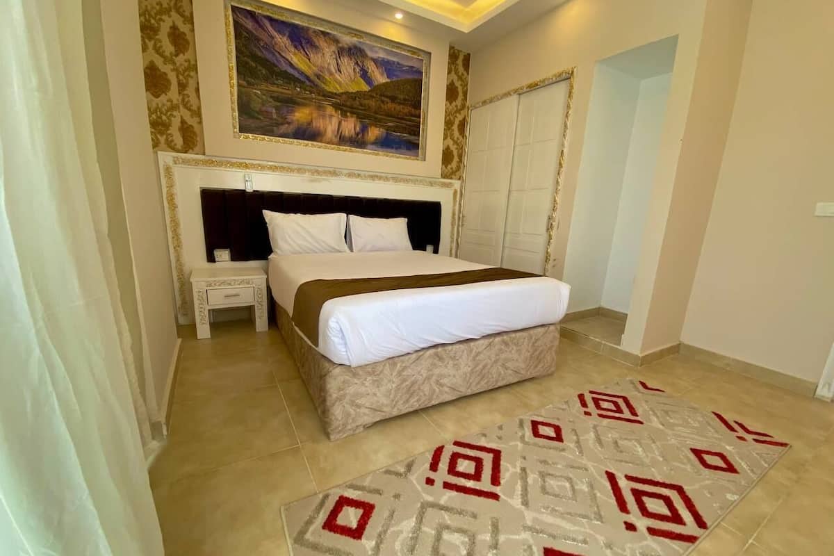 A bedroom with a bed, bedside table, and a painting on the wall.
