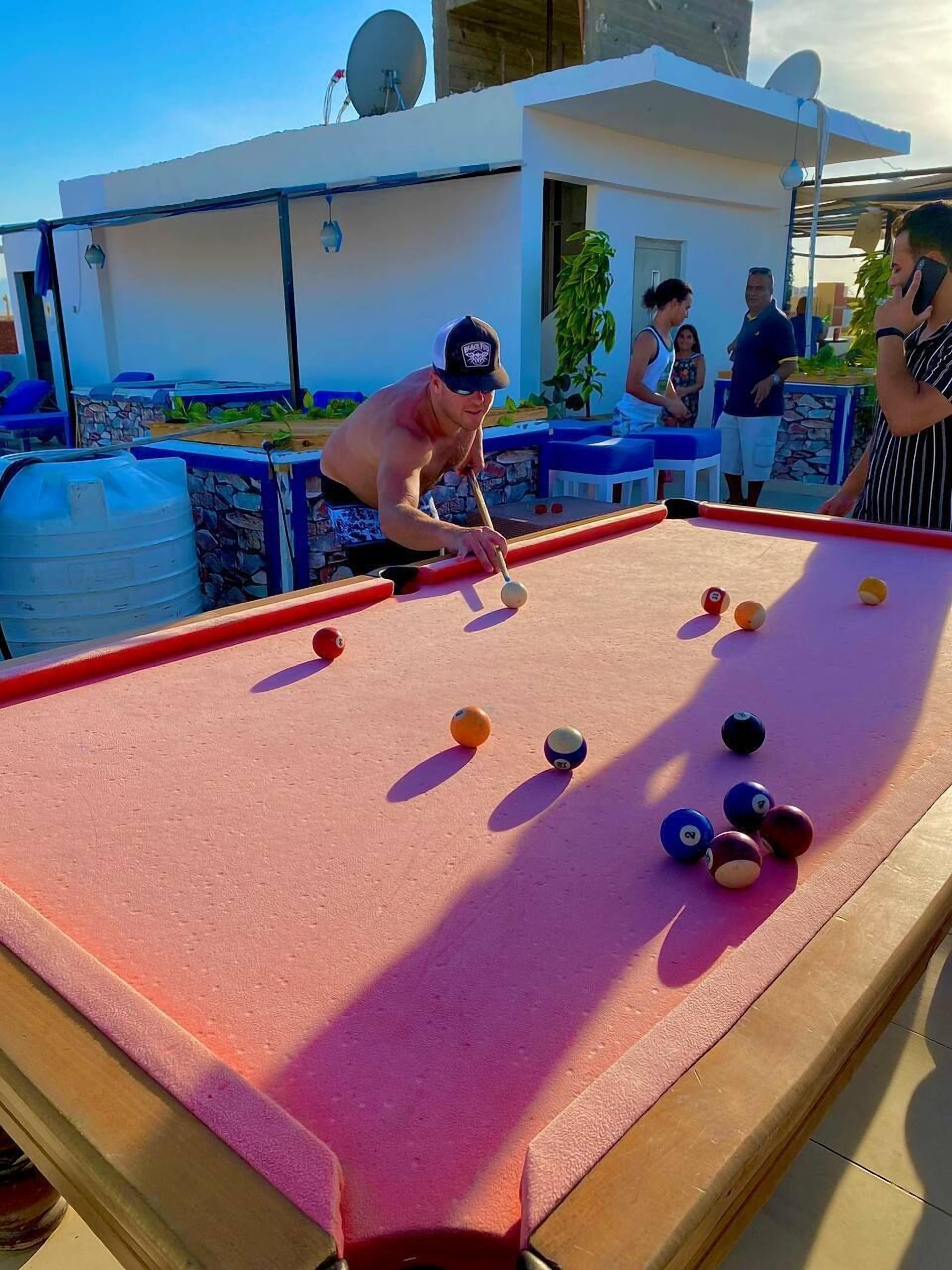 A pool table with balls, surrounded by people.